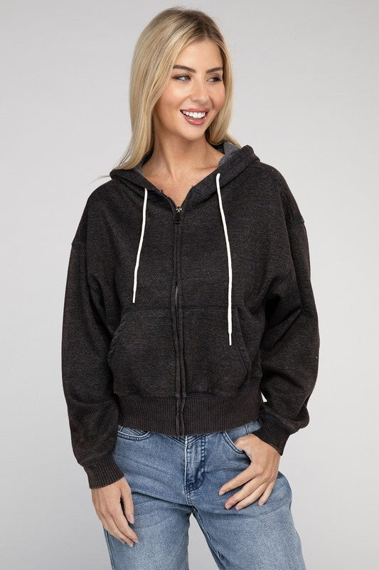 A smiling woman wearing a pink Acid Wash Cropped Zip-Up Hoodie and blue jeans, posing with one hand adjusting her hood.