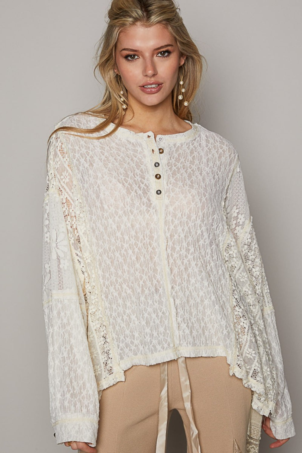 A woman is wearing the POL Round Neck Long Sleeve Raw Edge Lace Top, paired with beige pants, as she stands against a neutral background.