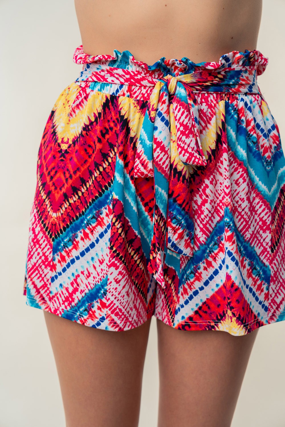 Close-up of a person wearing the White Birch High Waisted Printed Shorts, showcasing vibrant blue, pink, and yellow zigzag designs on lightweight slinky knit fabric with an adjustable waist-tie.