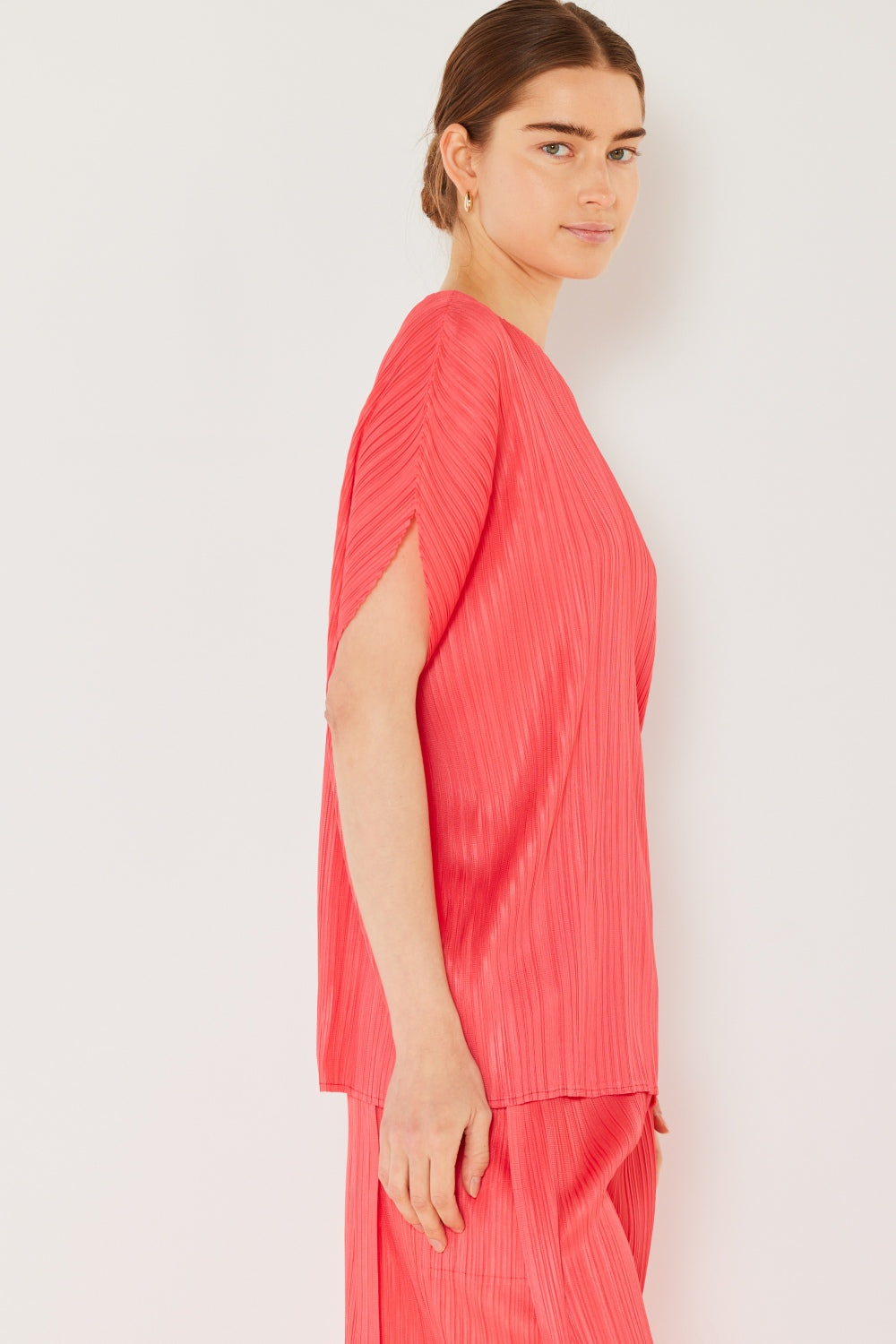 A person wearing the Marina West Swim Rib Pleated Oversized Dolman Sleeve Top in a fashionable light blue shade, paired with a brown belt and black skirt, stands against a plain background.