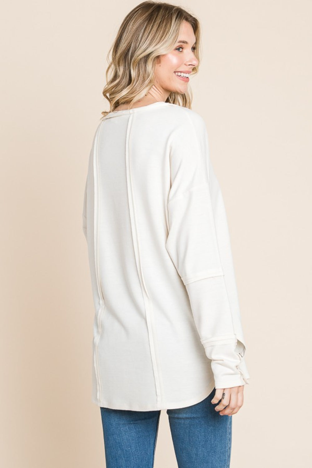 A person wearing the Culture Code Full Size V-Neck Dropped Shoulder Blouse, crafted from breathable fabric, poses against a beige background, highlighting the button details on the sleeves.