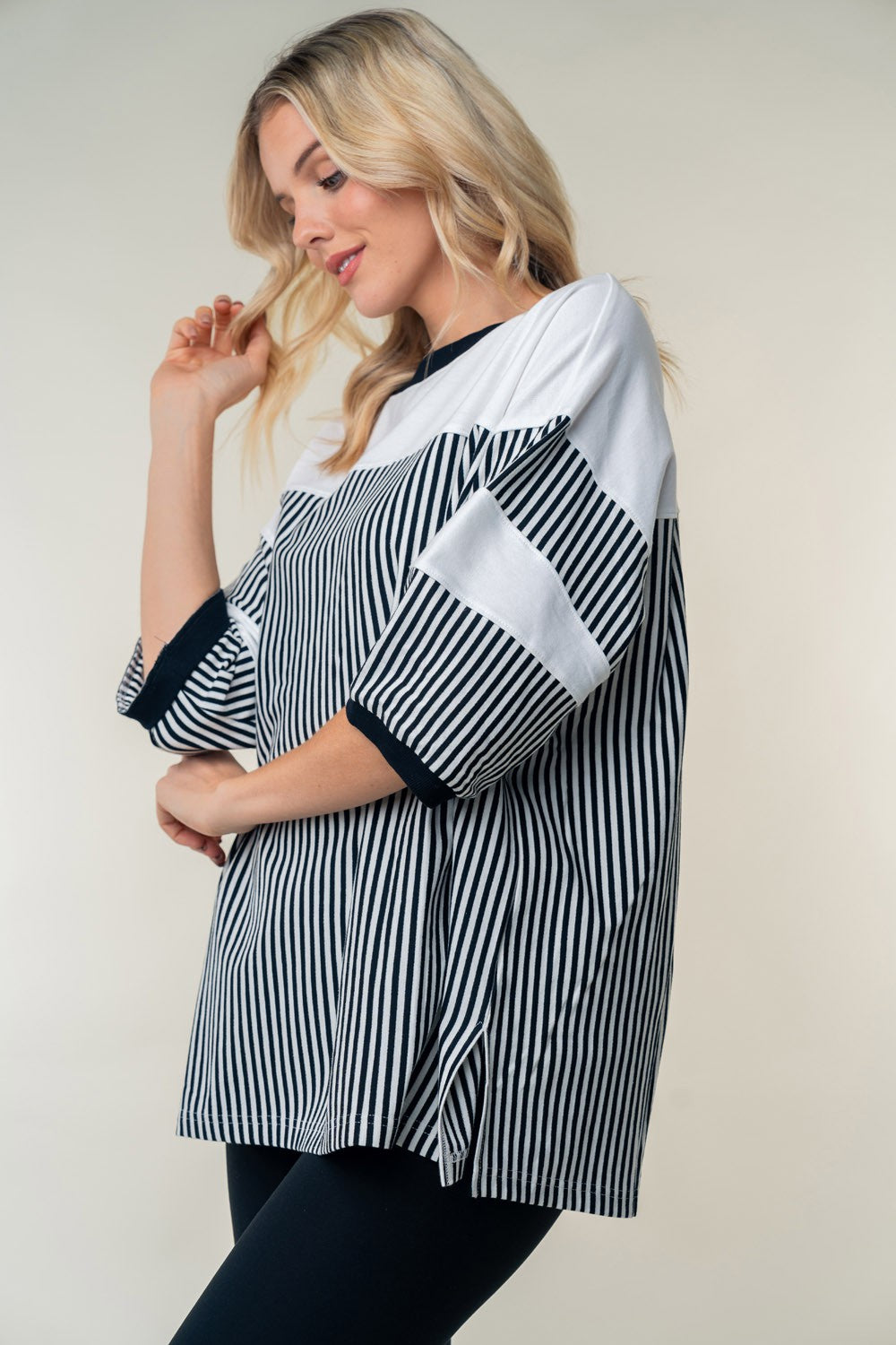 A woman with blonde hair wears the White Birch Full Size Striped Contrast Round Neck Top, posing with one hand near her head.