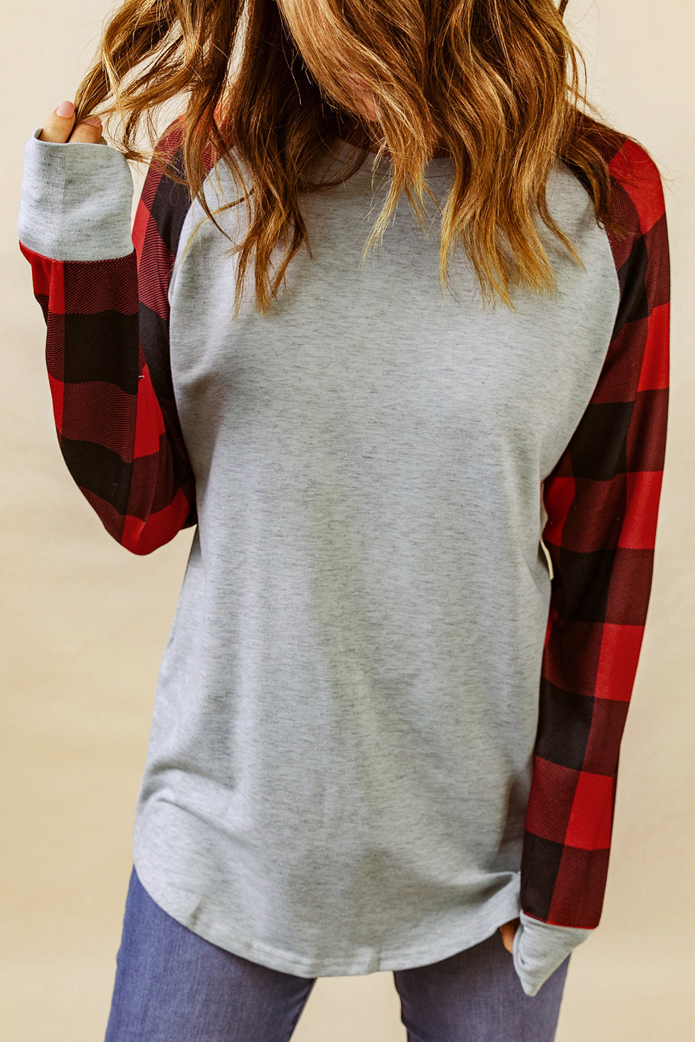 A person with wavy, brown hair is standing with their back to the camera, wearing a Gray Buffalo Plaid Long Sleeve Sweatshirt and blue jeans.