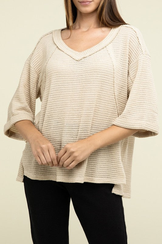 A person is dressed in a Brushed Waffle Exposed-Seam 3/4 Sleeve Top and white shorts, perfect for a casual wardrobe. They stand against a plain background, effortlessly embodying relaxed style.