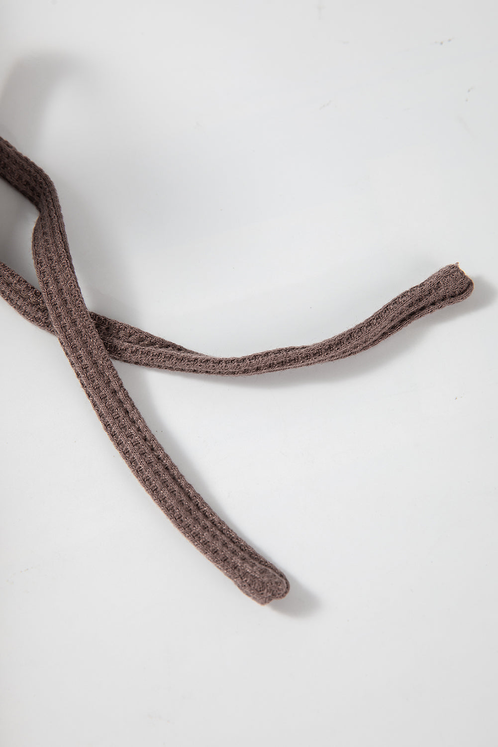 A woman with long hair is standing in profile, wearing a Coffee Waffle Knit Fleece Lined High Low Oversized Hoodie and black shorts. The background is a plain light gray.