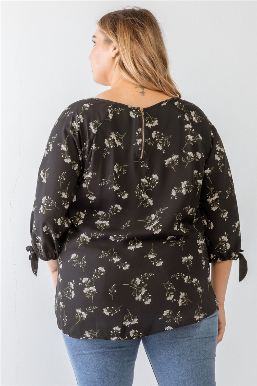 A person wearing a Zenobia Plus Size Floral Round Neck Blouse and blue jeans stands against a plain background.