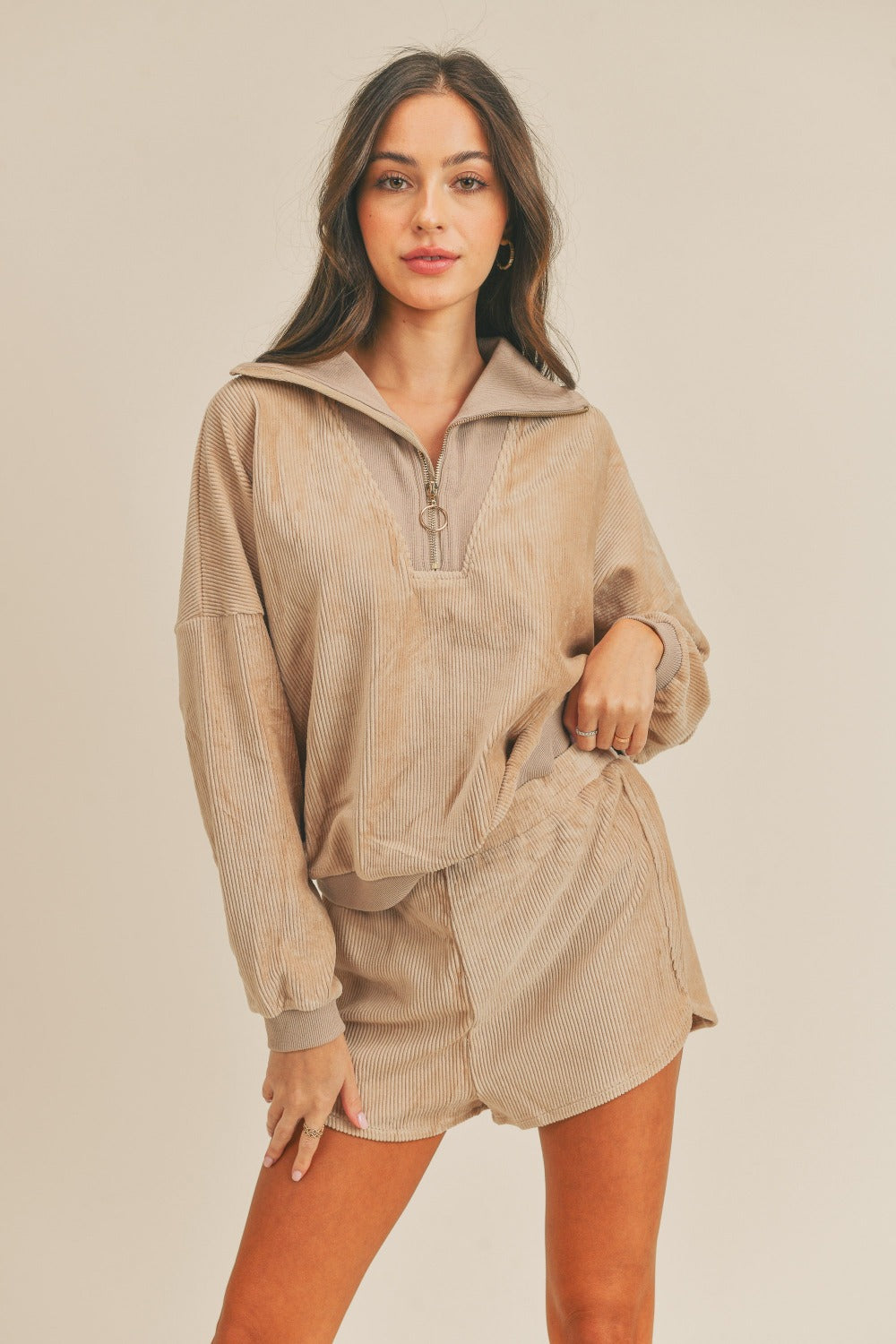 A woman stands confidently, wearing the MABLE Corduroy Half Zip Top and Shorts Set in a matching beige color, with her hands on her hips against a neutral background, effortlessly exuding retro charm.