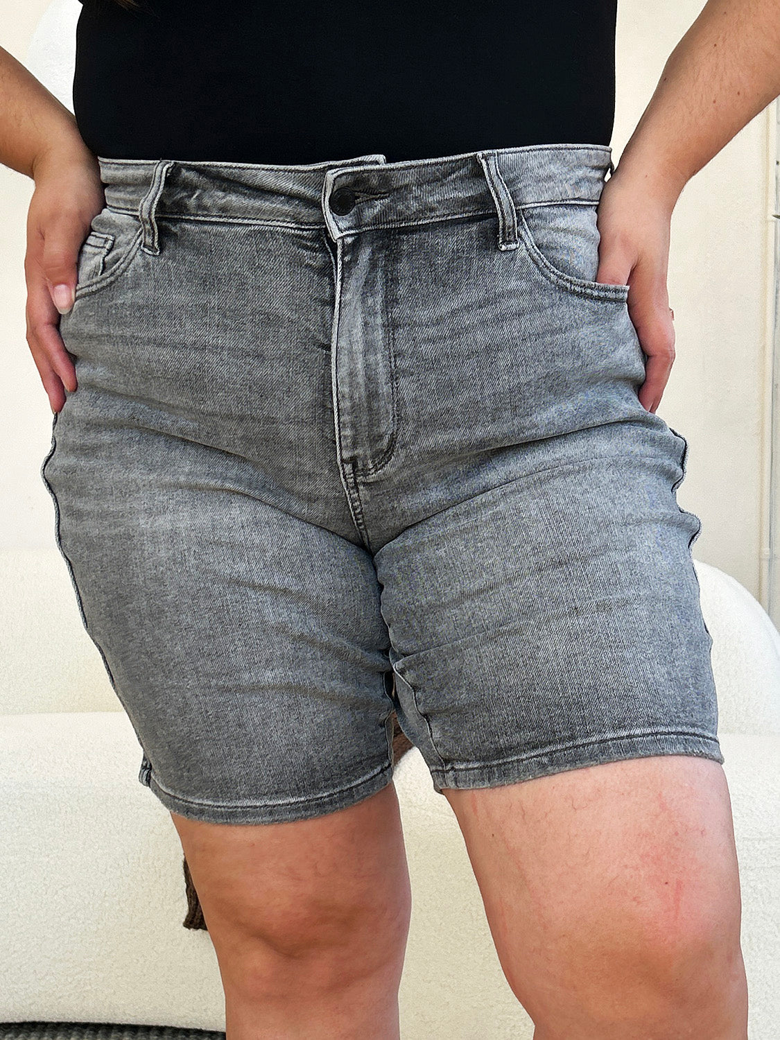 A person wearing a white top and the Judy Blue Full Size High Waist Washed Denim Shorts with vintage charm has one hand in their pocket. The shorts, featuring a faded design and belt loops, contribute to a retro-inspired look.