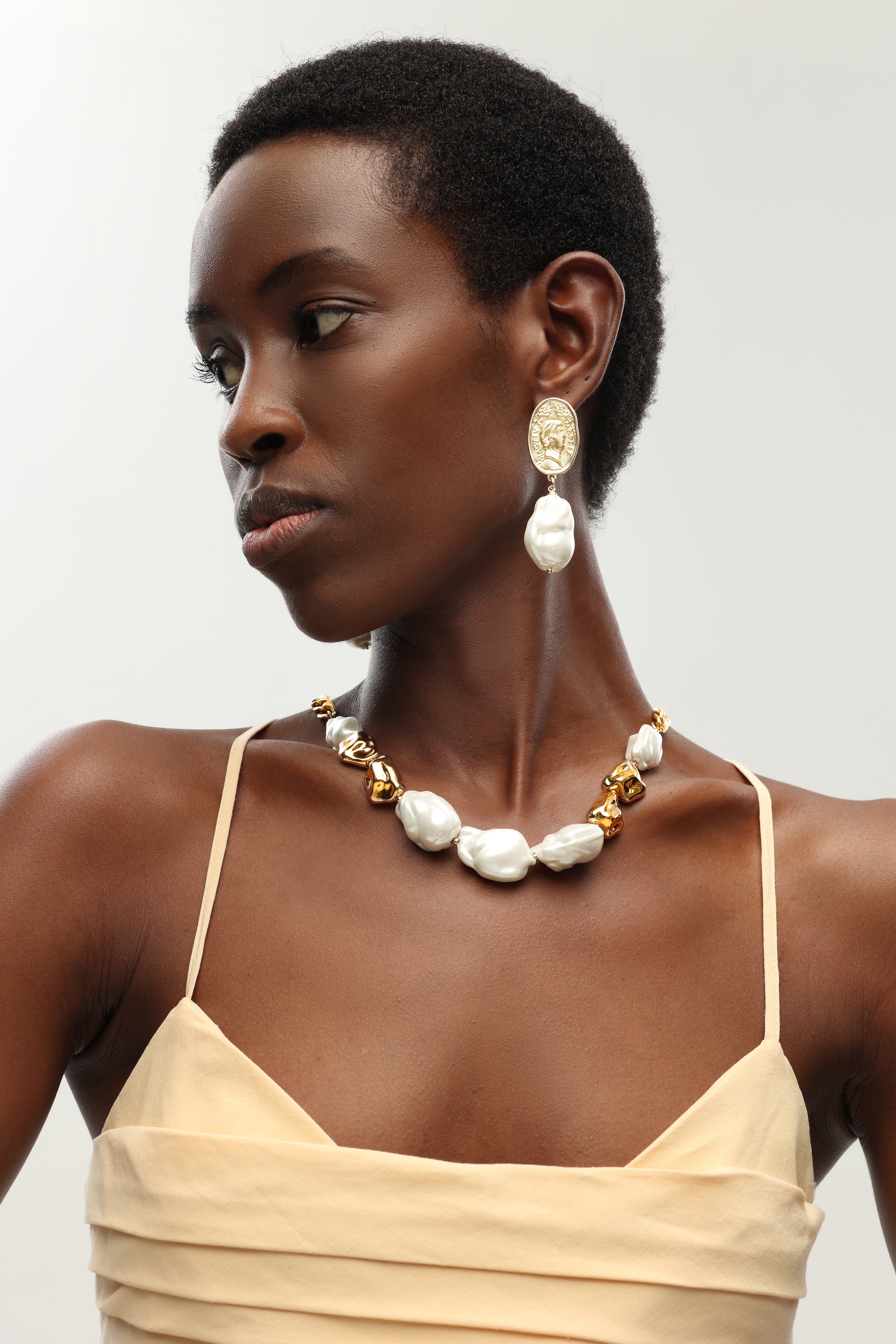 A pair of earrings featuring Matted Gold Sculpted Oversized Baroque Pearl Drop Earrings.