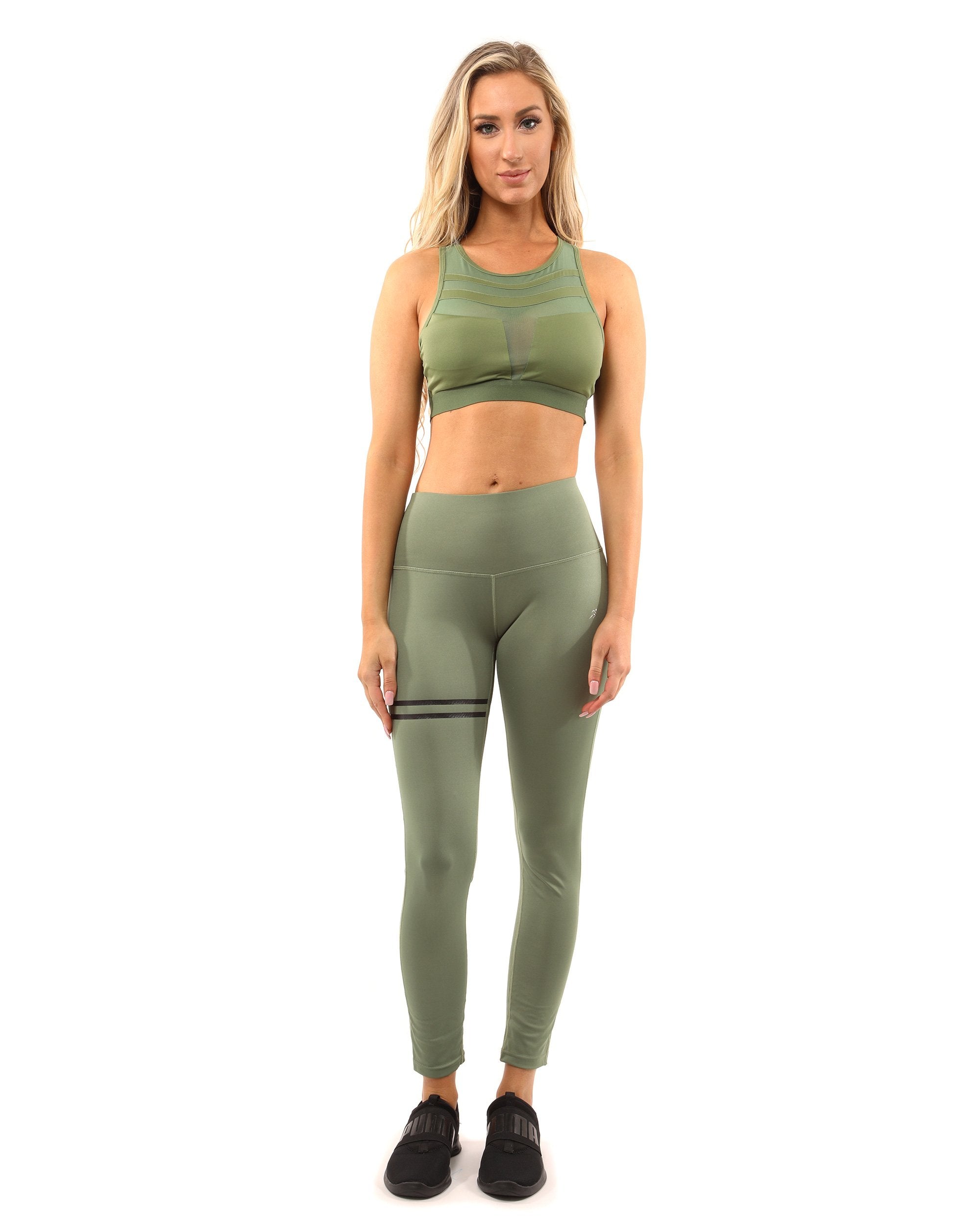 A person stands facing forward in the Huntington Set - Leggings & Sports Bra in Olive Green, paired with black shoes against a white background.