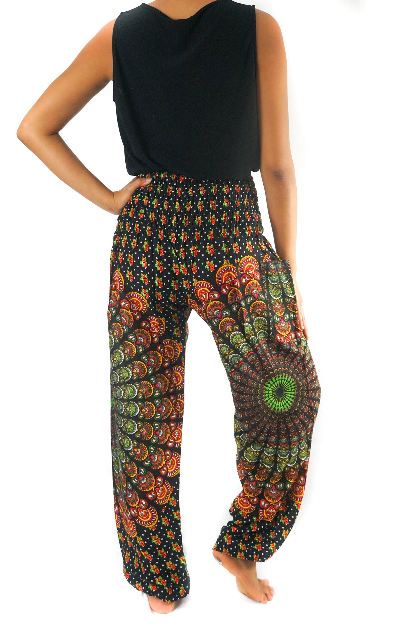 A person stands barefoot, wearing a unisex sleeveless black top and the brightly patterned, colorful high-waisted "Black Chakra Harem Pants, Hippie Pants, Boho Pants" made from 100% Rayon.