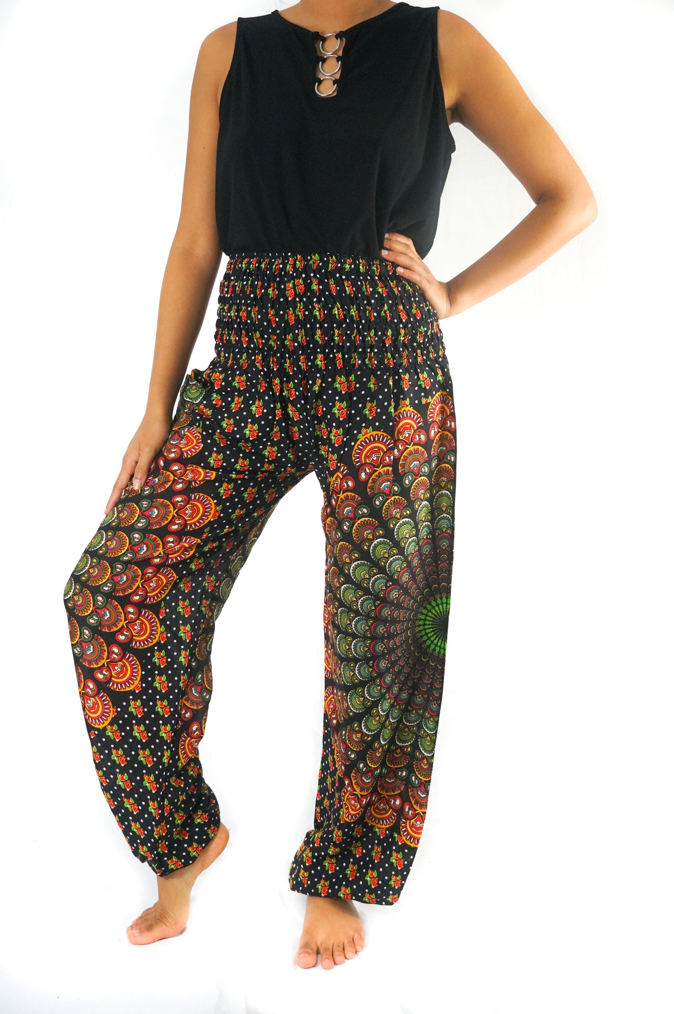 A person stands barefoot, wearing a unisex sleeveless black top and the brightly patterned, colorful high-waisted "Black Chakra Harem Pants, Hippie Pants, Boho Pants" made from 100% Rayon.