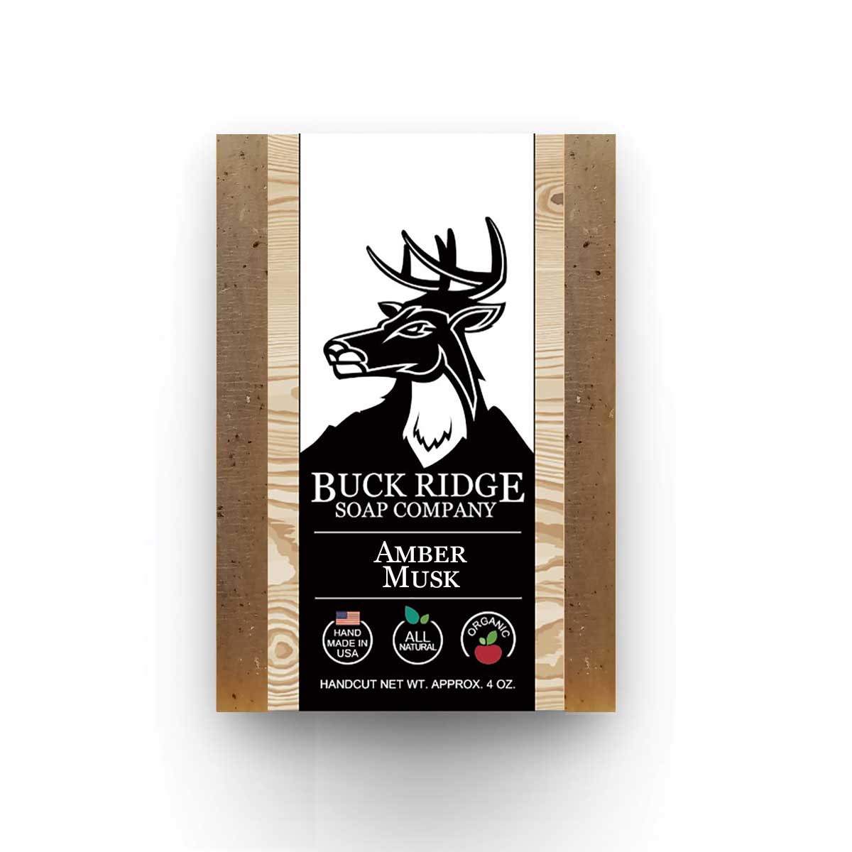 The packaging of Amber Musk Handmade Soap by Buck Ridge Soap Company highlights its enchanting unisex fragrance, suitable for all. It features a deer logo along with icons indicating that it's handmade, all-natural, and organic. The soap is enriched with turmeric powder for added advantages and has an approximate net weight of 4 oz.