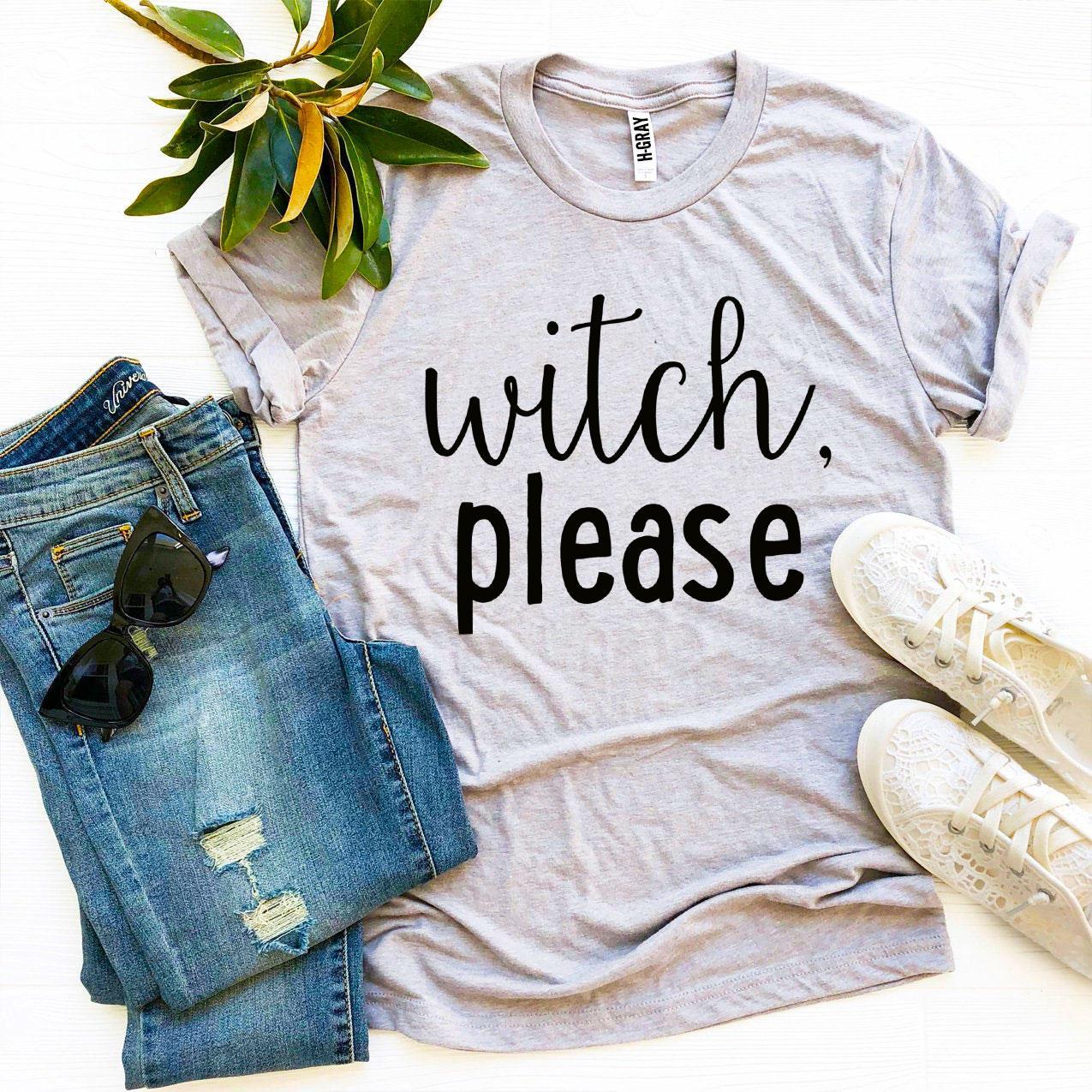 A Witch Please T-shirt in gray, celebrated for its soft texture and comfortable retail fit, is beautifully laid out next to a pair of blue jeans, beige high heels, and a bouquet of flowers.