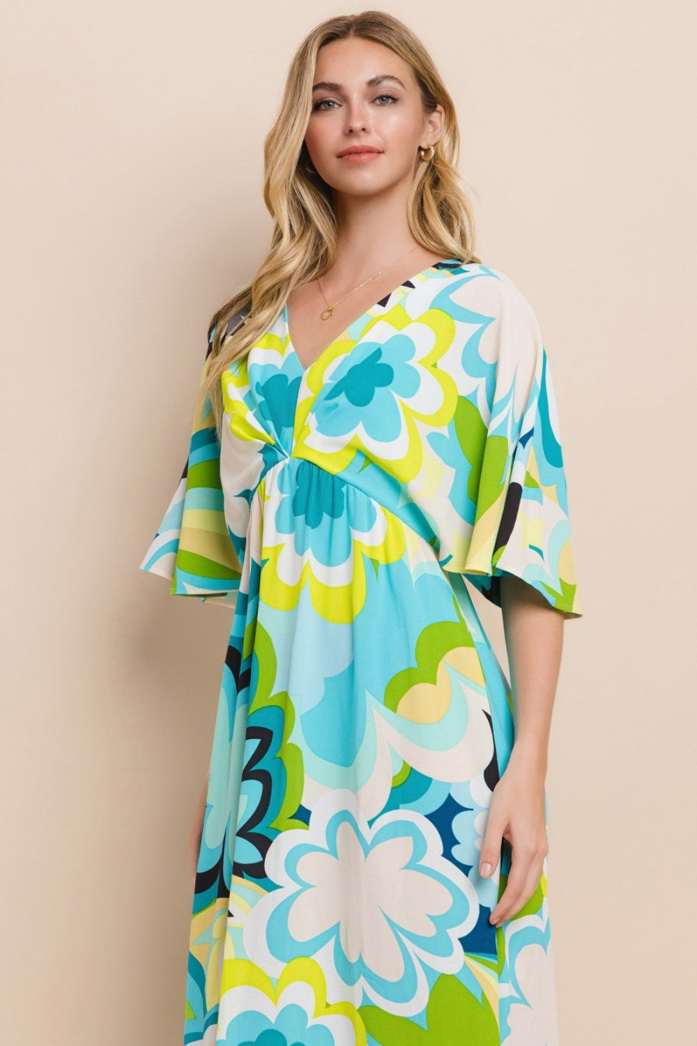 Against a simple backdrop, a woman models the ODDI Floral Printed Slit Maxi Dress, exuding a sense of versatile elegance. This maxi dress embodies summer chic with its vibrant floral design featuring shades of blue, green, and yellow.