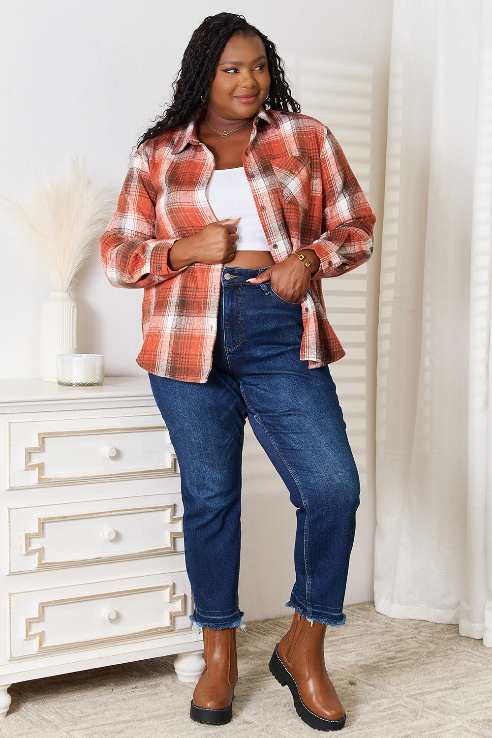 A woman in a Plaid Collared Neck Long Sleeve Shirt and blue jeans stands indoors, smiling and looking downward. She is wearing a white top underneath the classic wardrobe staple.