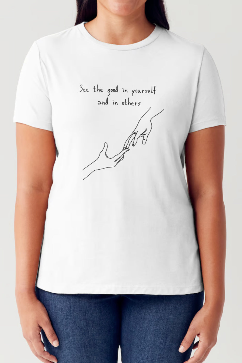 A person is wearing a Simply Love Full Size Slogan Graphic Short Sleeve Tubular T-Shirt, featuring a minimalist design of two hands reaching for each other. The text reads: "See the good in yourself and in others," delivering a positive message to all who see it.