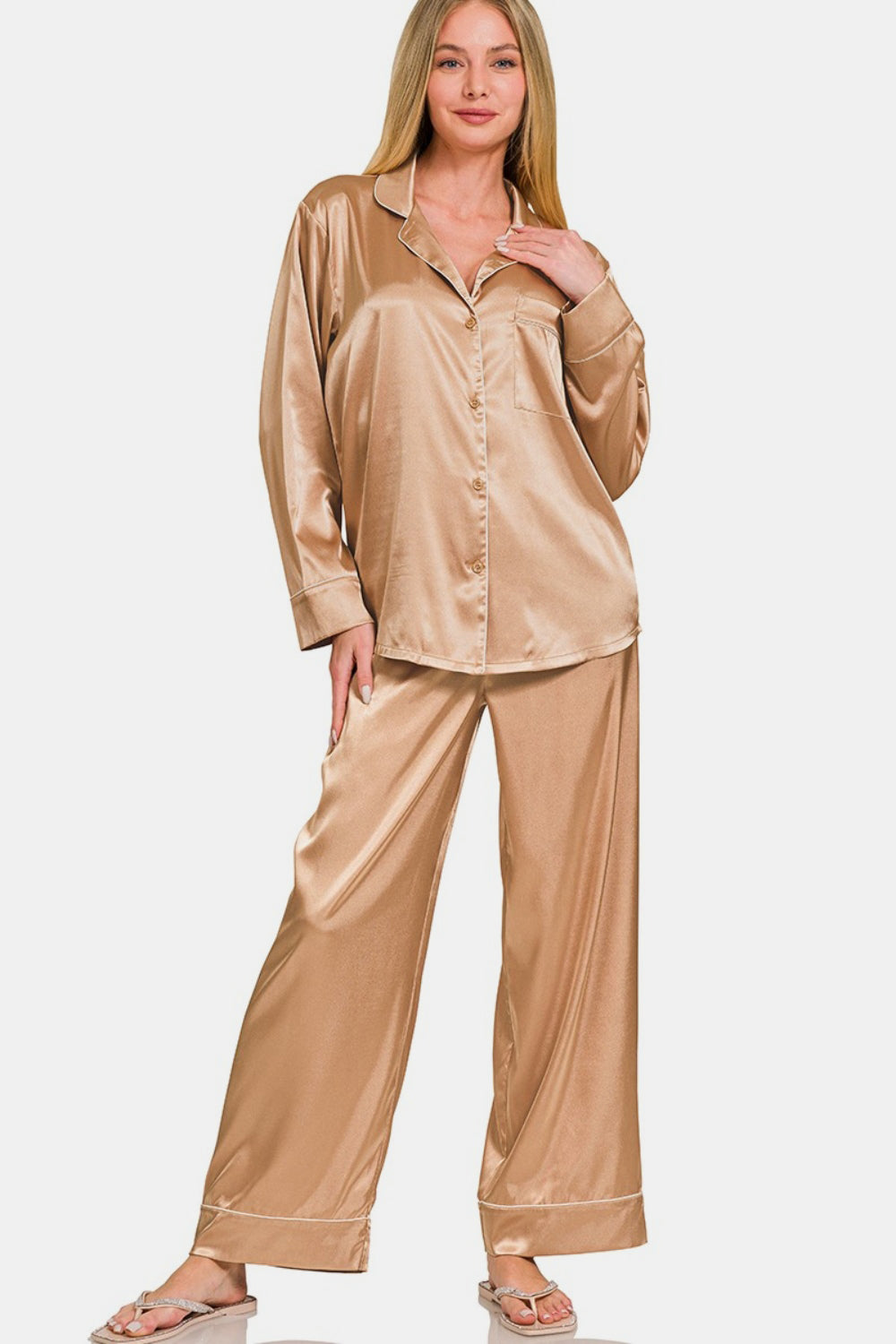 The woman stands elegantly in the Zenana Satin Long Sleeve Shirt and Pants Pajama Set, her hand resting on the collar of the shirt, complementing the ensemble’s elastic waist pants.