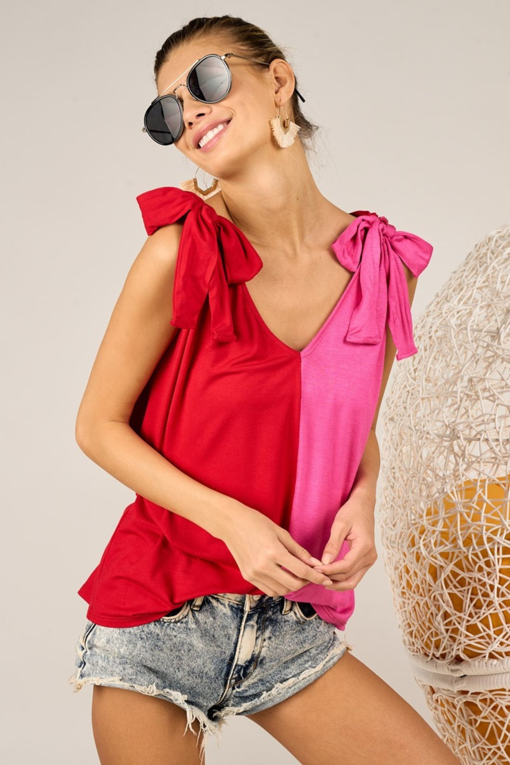 A person wearing the stylish BiBi Shoulder Ribbon Tied Contrast Tank, paired with denim shorts, sunglasses, and earrings, poses against a neutral background.