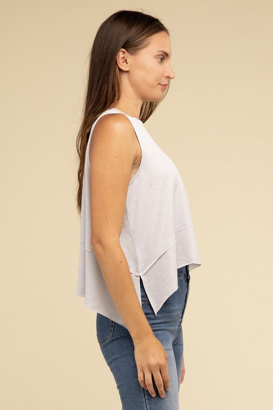 Wearing the Shark Bite Side Slit Short Sleeveless Top in maroon paired with white pants, a model is set against a beige background, exemplifying an effortlessly chic and casual wardrobe.