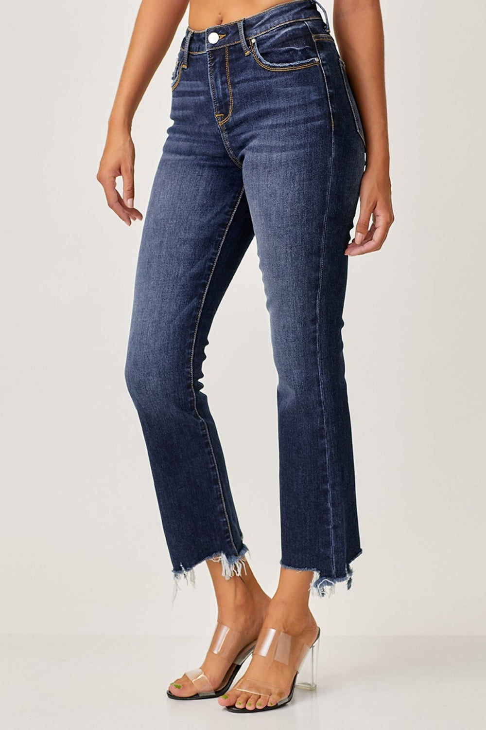 A person striking a pose in Risen Full Size Frayed Hem Cropped Straight Jeans with clear high-heeled sandals, one hand casually tucked in a pocket against a plain background.