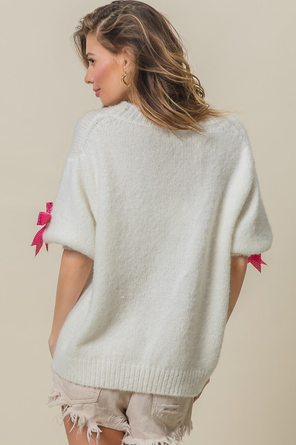 A woman wearing a striking and fashionable BiBi Sequin Bow Puff Sleeve Sweater, paired with light-colored shorts, stands against a plain background.