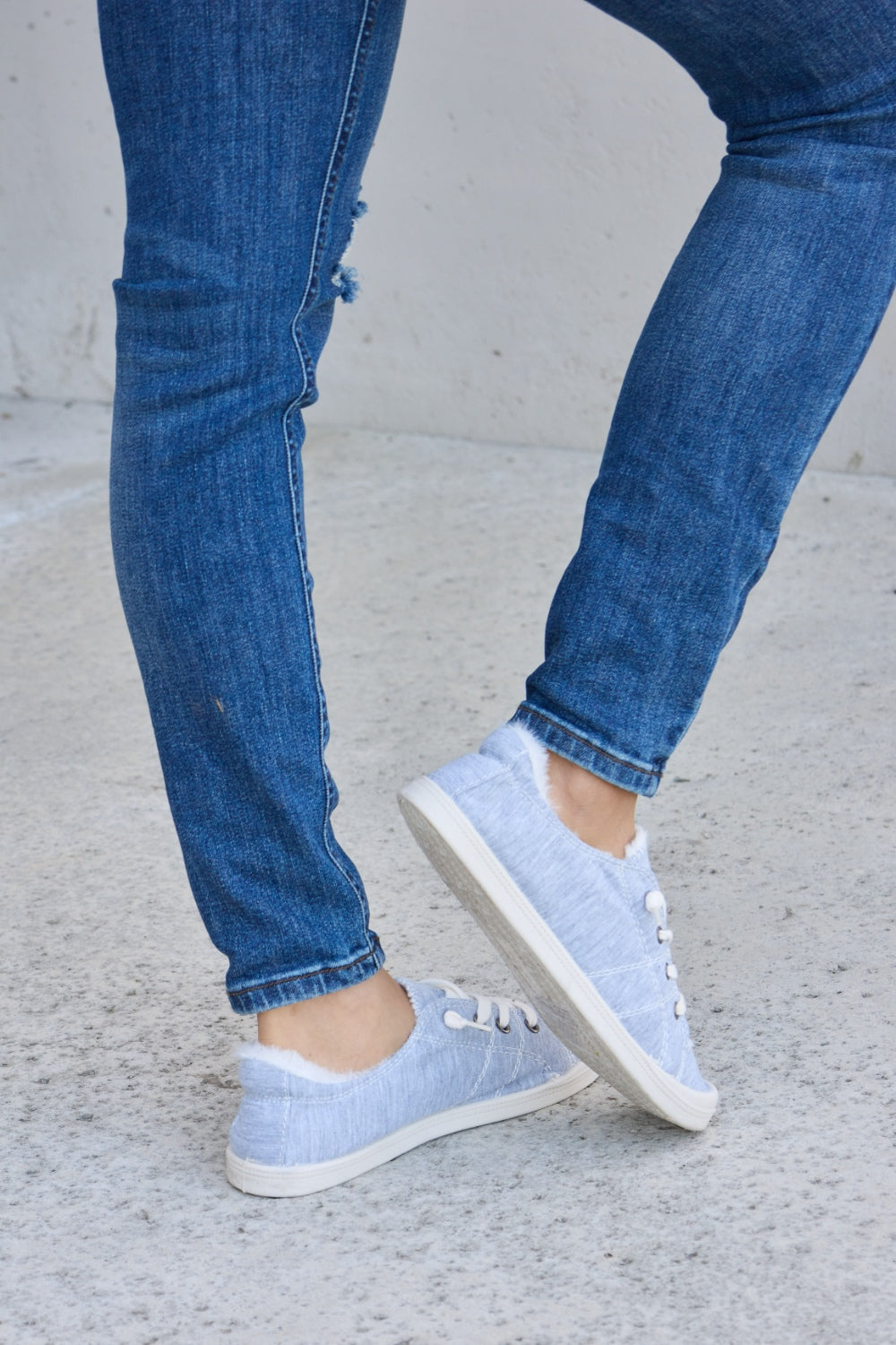 Person wearing ripped blue jeans and Forever Link Lace-Up Plush Thermal Flat Sneakers in grey with white laces, standing on a concrete surface.