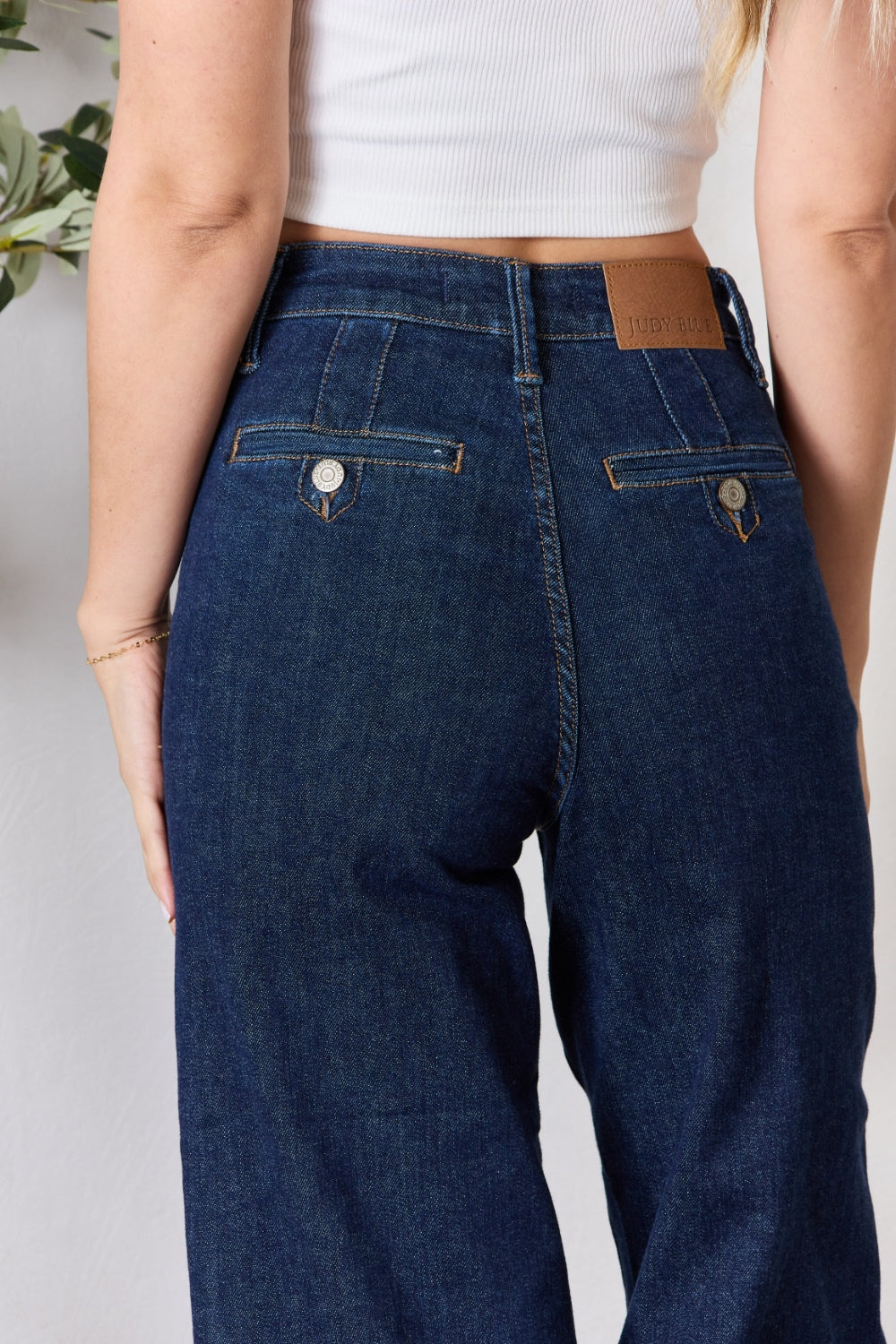 A person wearing the Judy Blue Full Size High Waist Cropped Wide Leg Jeans, which are renowned for their tummy control design, and nude block heel sandals stands near a potted plant.