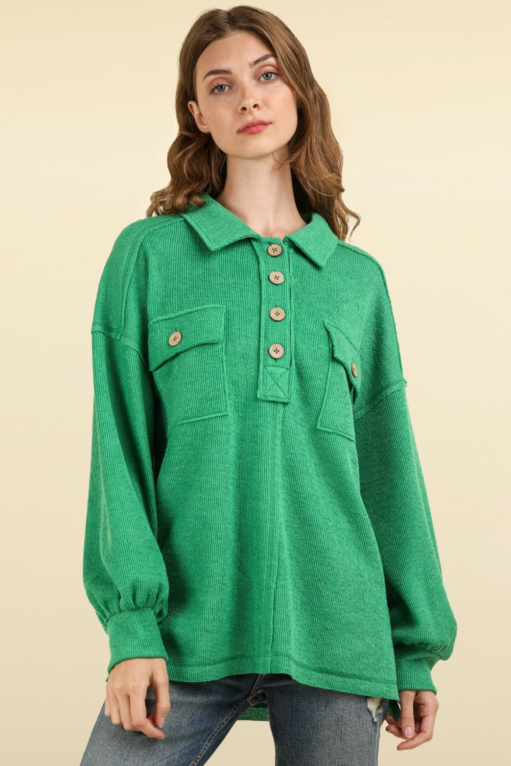 A person with long hair wearing an oversized fit, green VERY J Collared Half Button Knit Top with Pockets stands against a beige background.