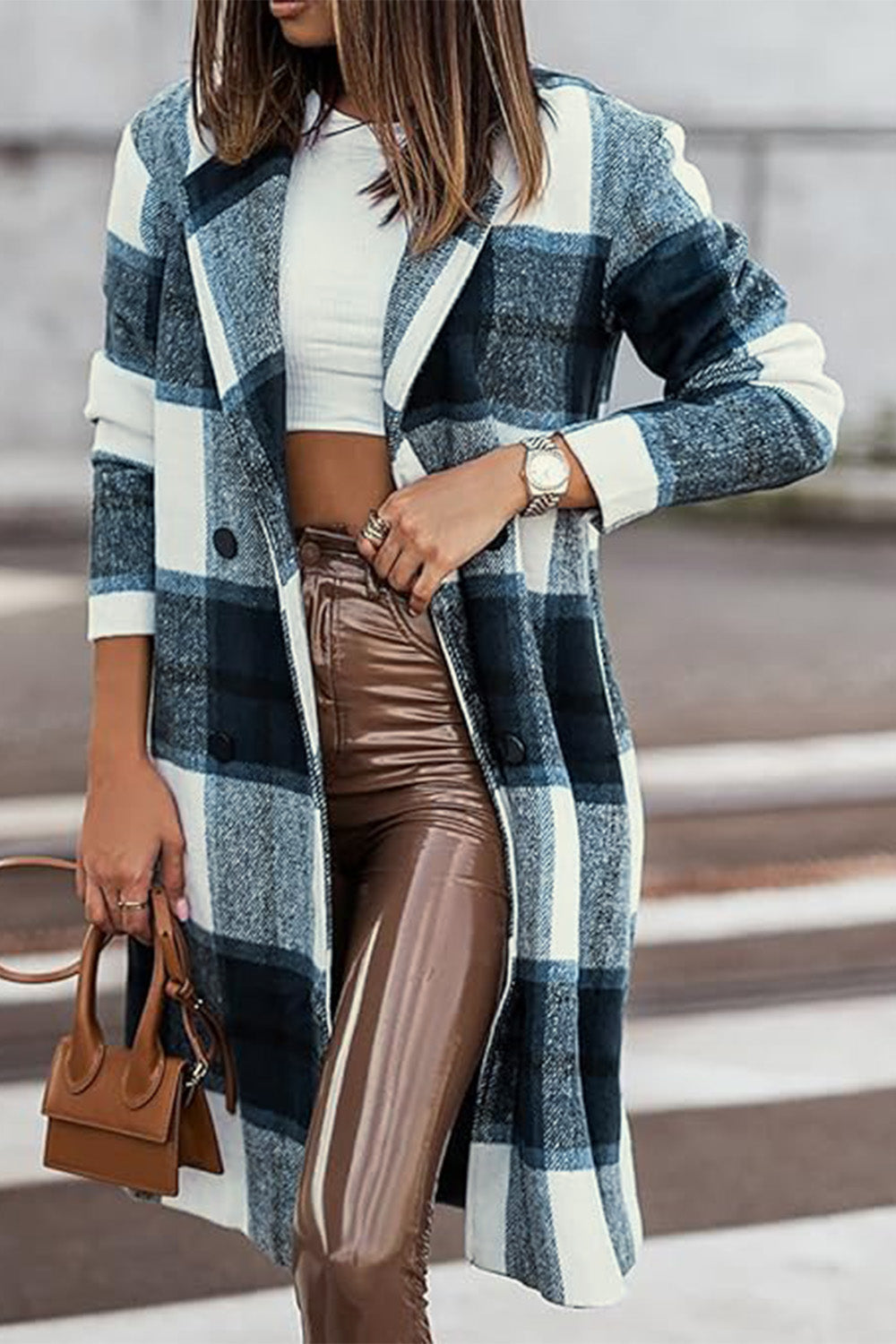 A woman stands on a sidewalk wearing the Double Take Full Size Plaid Button Up Lapel Collar Coat in pink and white over a white top and blue jeans, with her right hand lightly touching her hair. The polyester fabric of the coat makes it durable and perfect for an easy machine wash cold.