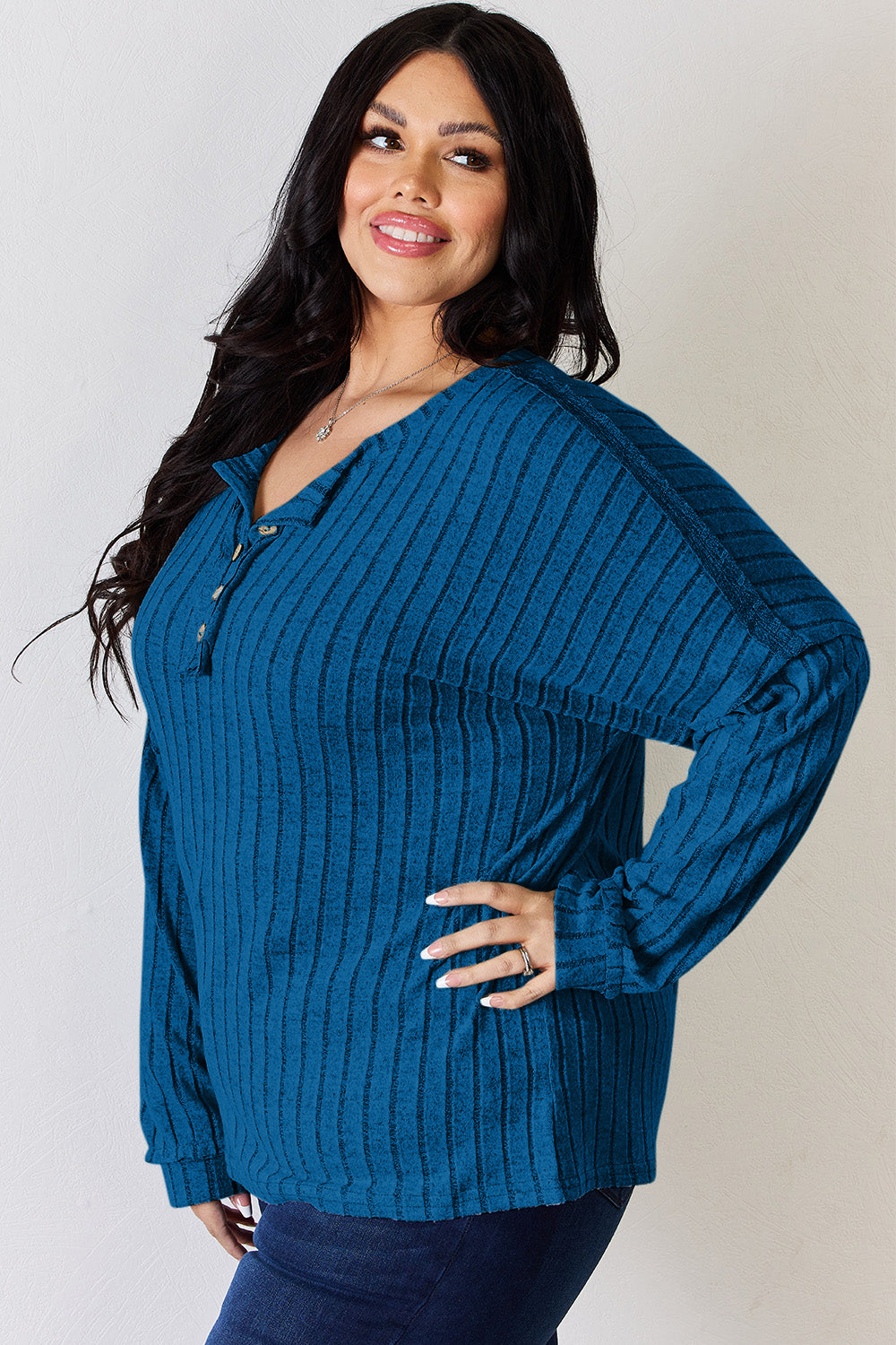 A woman with long, wavy blonde hair wears a slightly stretchy, textured Basic Bae Full Size Ribbed Half Button Long Sleeve T-Shirt in pink, standing against a neutral backdrop.