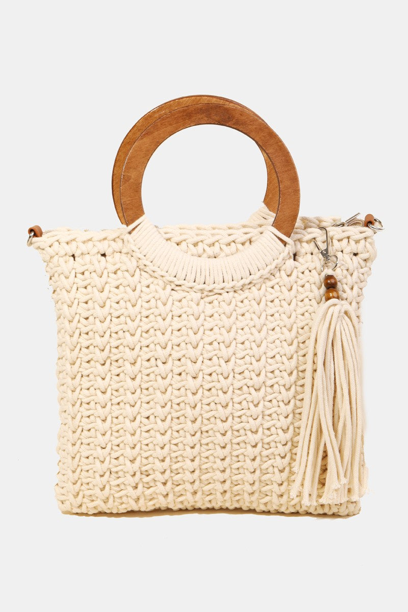 The Fame Crochet Knit Convertible Tote Bag includes a cream-colored design with round wooden handles and a matching tassel accent.