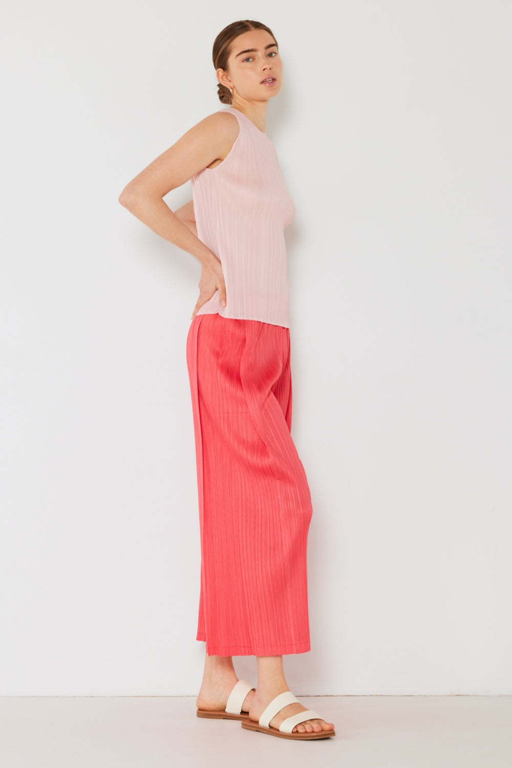 A person wearing the Marina West Swim Pleated Wide-Leg Pants with side pleat detail in red, standing against a white background with hands in pockets and wearing white sandals.