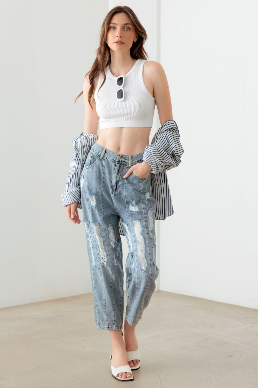 A person wearing Litz La Washed Barrel Leg High Waist Distressed Jeans and white sandals stands on a gray floor against a white wall.