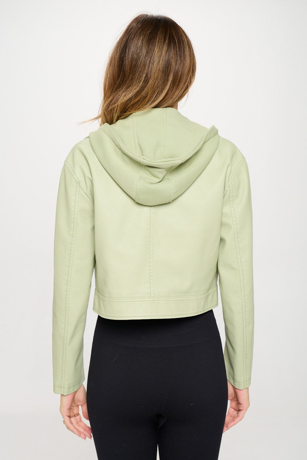 A person showcases a trendy Coalition LA Snap Down Cropped Hooded Jacket in light green over a sleek black outfit against a plain background.