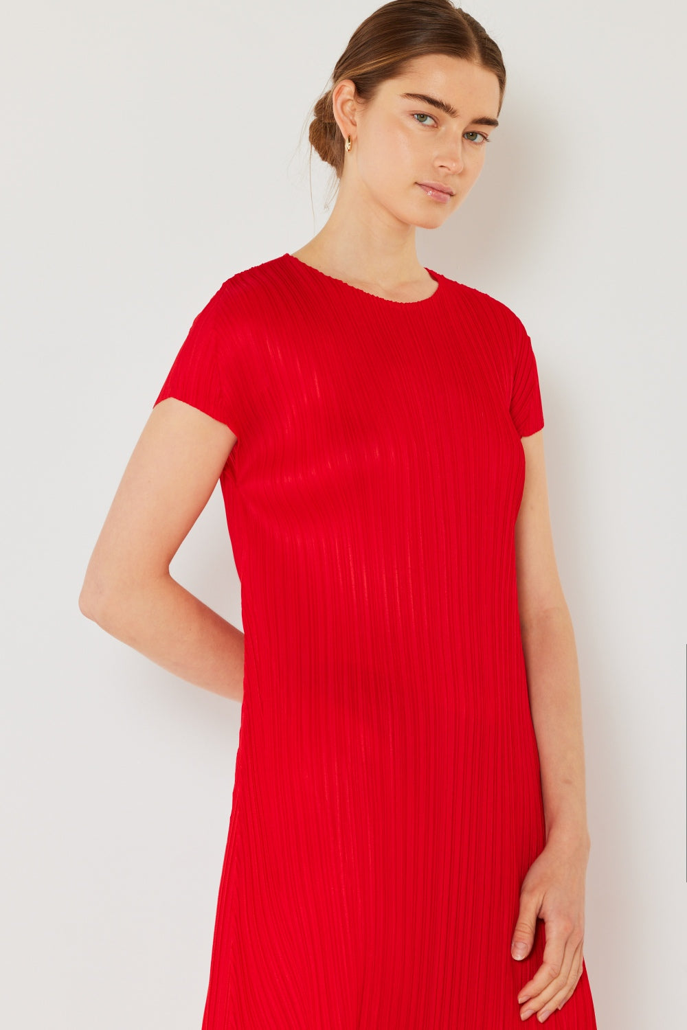 A person stands against a light wall, wearing an elegant Marina West Swim Pleated Cap Sleeve A-Line Dress in black and white sandals.