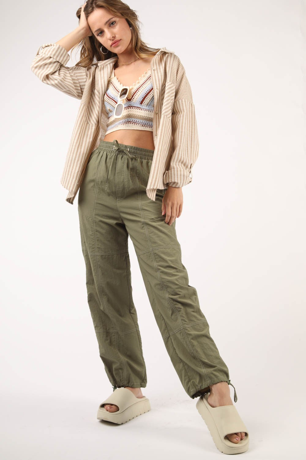 A person wearing VERY J Drawstring Woven Parachute Joggers in olive green and white sneakers stands against a plain background, showcasing the seamless blend of style and comfort with intricate woven fabric details.