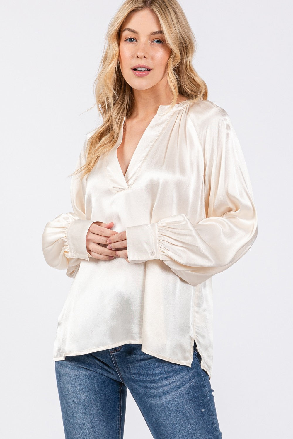 A person is wearing a SAGE + FIG Notched Long Sleeve Blouse in cream-colored satin paired with blue jeans.