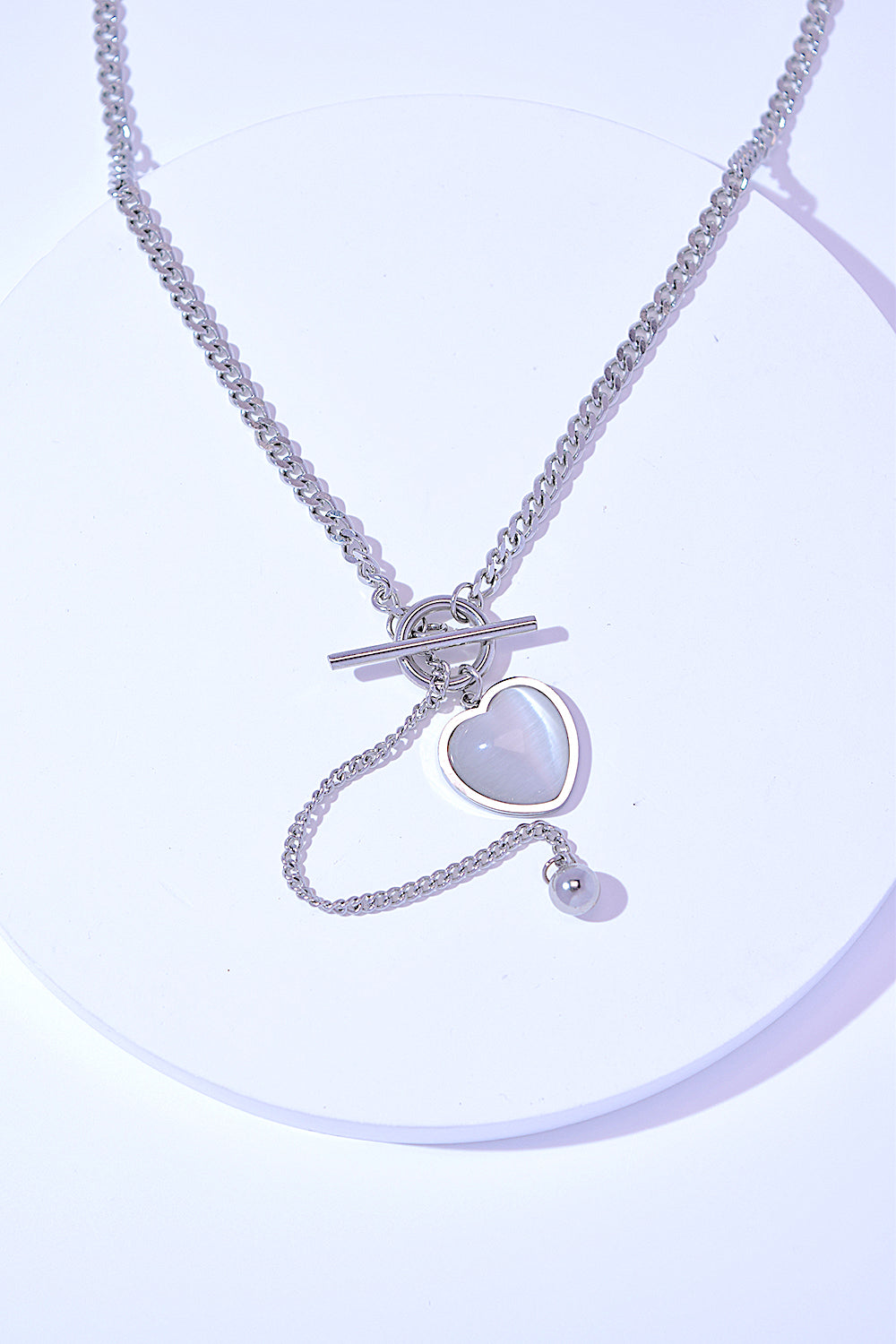 A Titanium Steel Heart Necklace with a heart-shaped pendant and a small key charm, featuring a delicate cat's eye stone, on a white background.