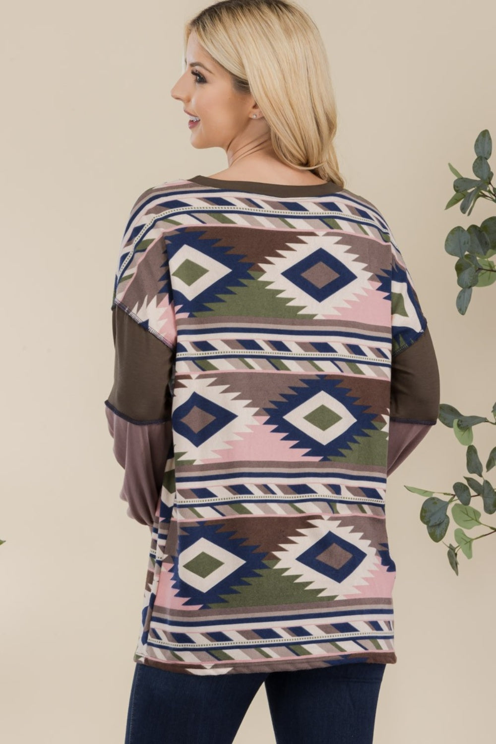 A woman with long blonde hair is wearing the Celeste Full Size Exposed Seam Printed Color Block T-Shirt and dark jeans, standing in front of a neutral background.