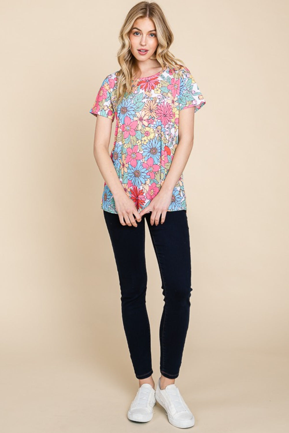 A woman wearing a vibrant BOMBOM Floral Short Sleeve T-Shirt and dark pants, posing against a beige background.