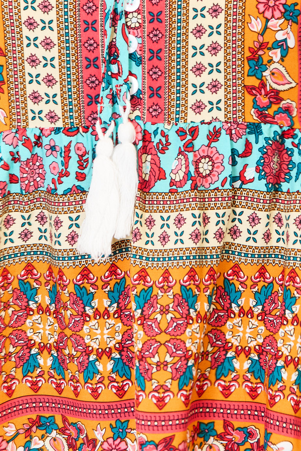 A woman wearing the Devine Bohemian Tassel Tie Puff Sleeve Babydoll Blouse, adorned with a mix of vibrant floral designs, smiles in her jeans while standing indoors against a light background.