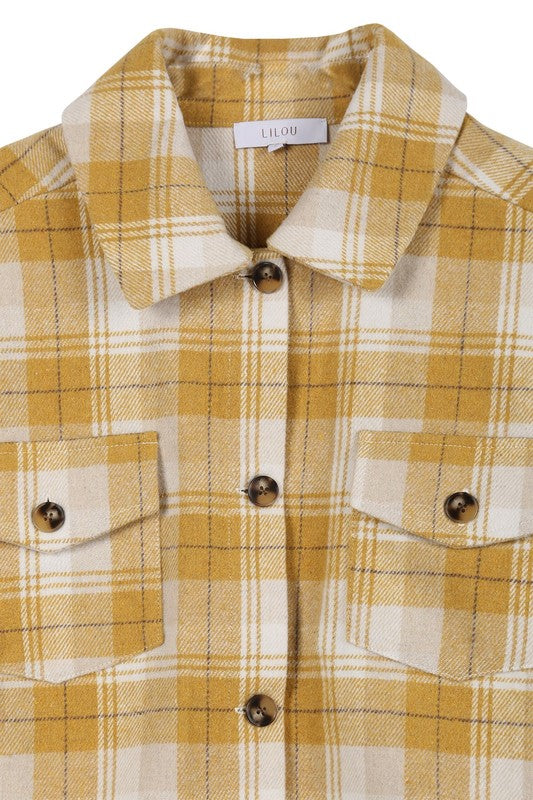 A person wearing a yellow plaid short shacket with pockets and blue jeans, highlighted by a crisp shirt collar, sits against a neutral backdrop.