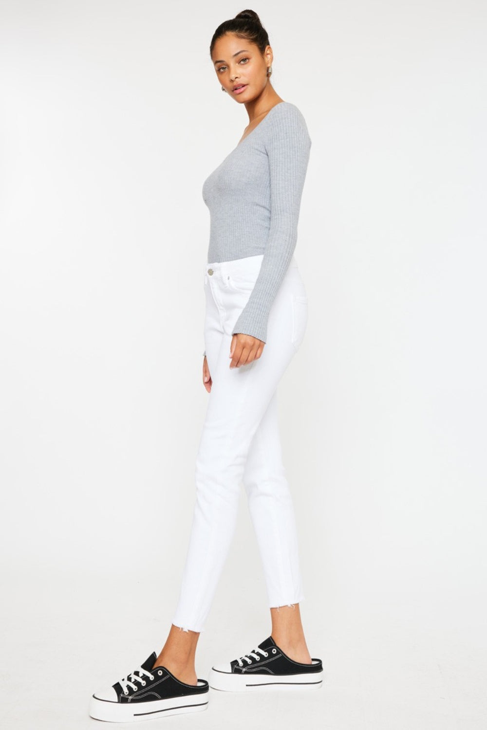 A person models a versatile gray long-sleeve top paired with flattering fit Kancan Mid Rise Ankle Skinny Jeans and sleek black sneakers, all set against a pristine white background.