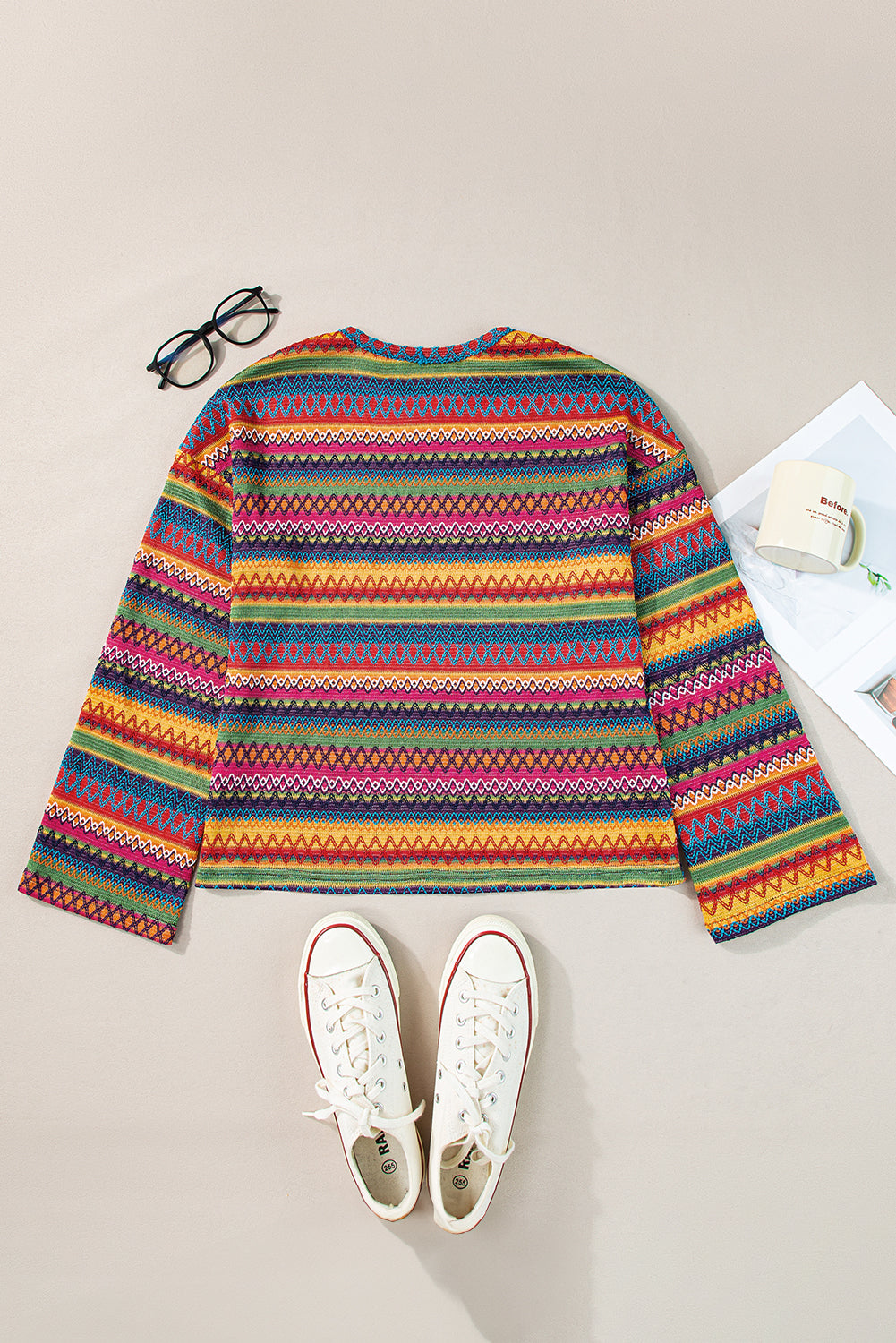 A person stands with hands in the pockets of their denim shorts, wearing a colorful Rose Red Ethnic Wavy Pattern Drop Shoulder Knit Top and a white shoulder bag.