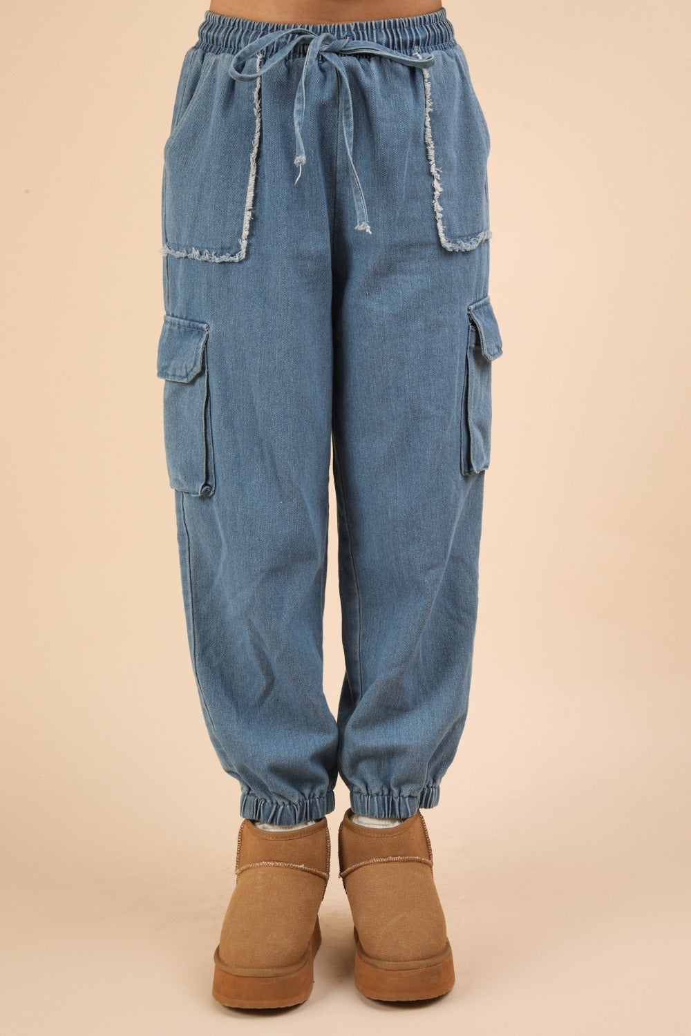 The individual is wearing VERY J Washed Drawstring Jogger Cargo Jeans, which feature elasticated cuffs, large front and side pockets, a drawstring waist, and a fashionable washed finish. They have paired these jeans with tan-colored boots.