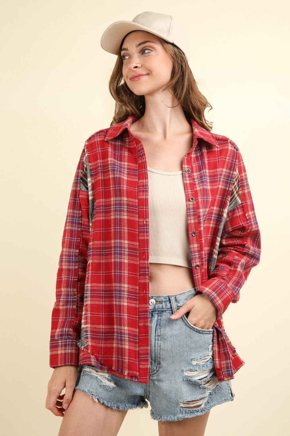 A woman wearing a VERY J Contrast Plaid Raw Detail Shirt, blue denim shorts, and a beige cap poses against a plain background.