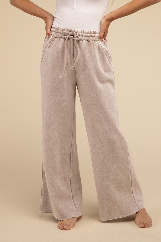 A person wearing acid wash fleece palazzo sweatpants with pockets paired with a white ribbed top, standing barefoot on a neutral background.