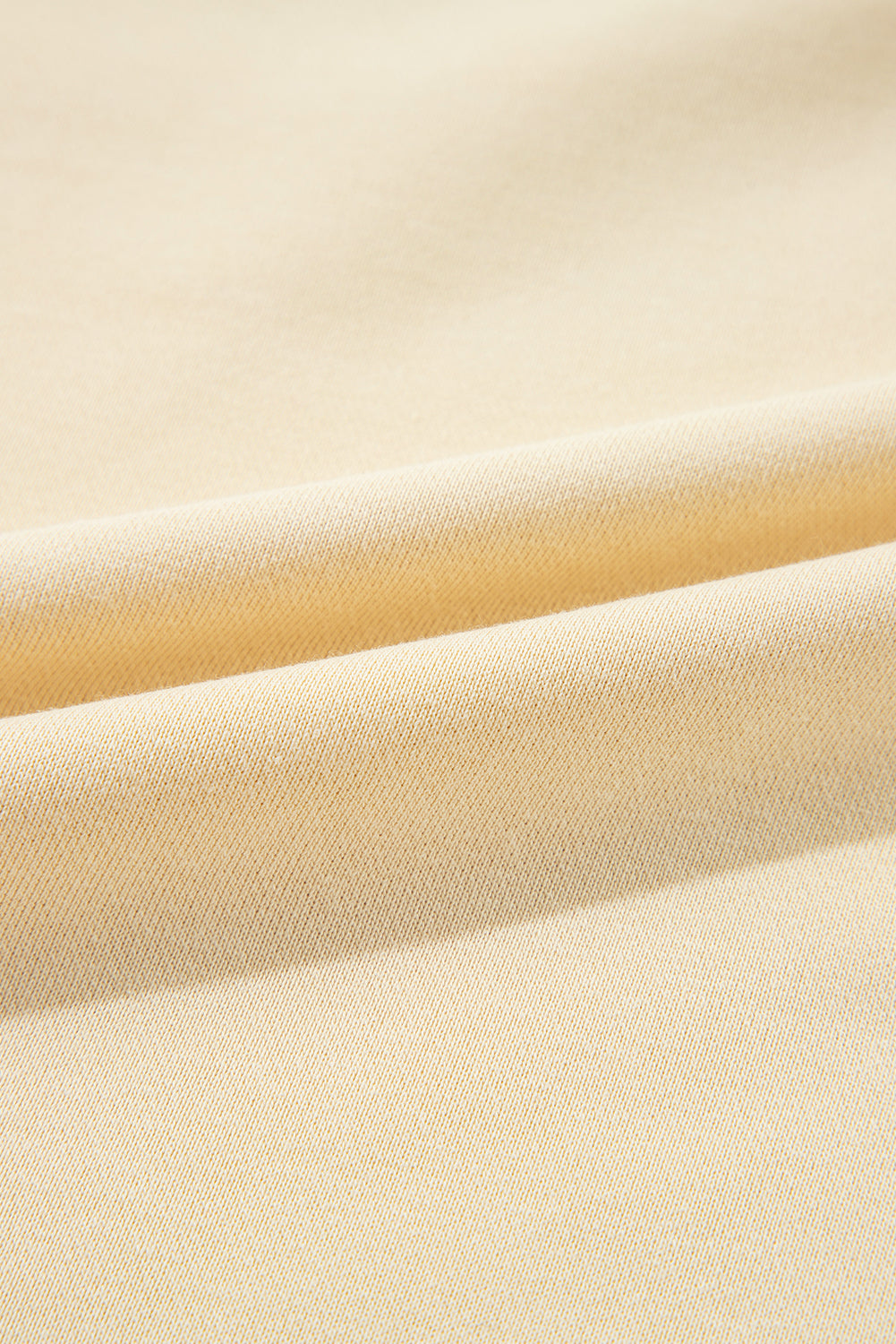 A woman with wavy hair stands with her back to the camera, wearing a Beige Splicing Round Neck Pullover Sweatshirt and blue jeans. She is in front of a white wall and a decorative plant, presenting a casual yet polished look.