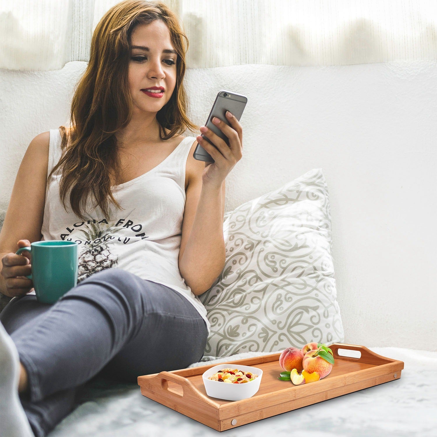 Bamboo Folding Bed Table Breakfast Tray with legs, holding a cup, fruits, a jar of nuts, and a plate with cheese and crackers, on a white background.